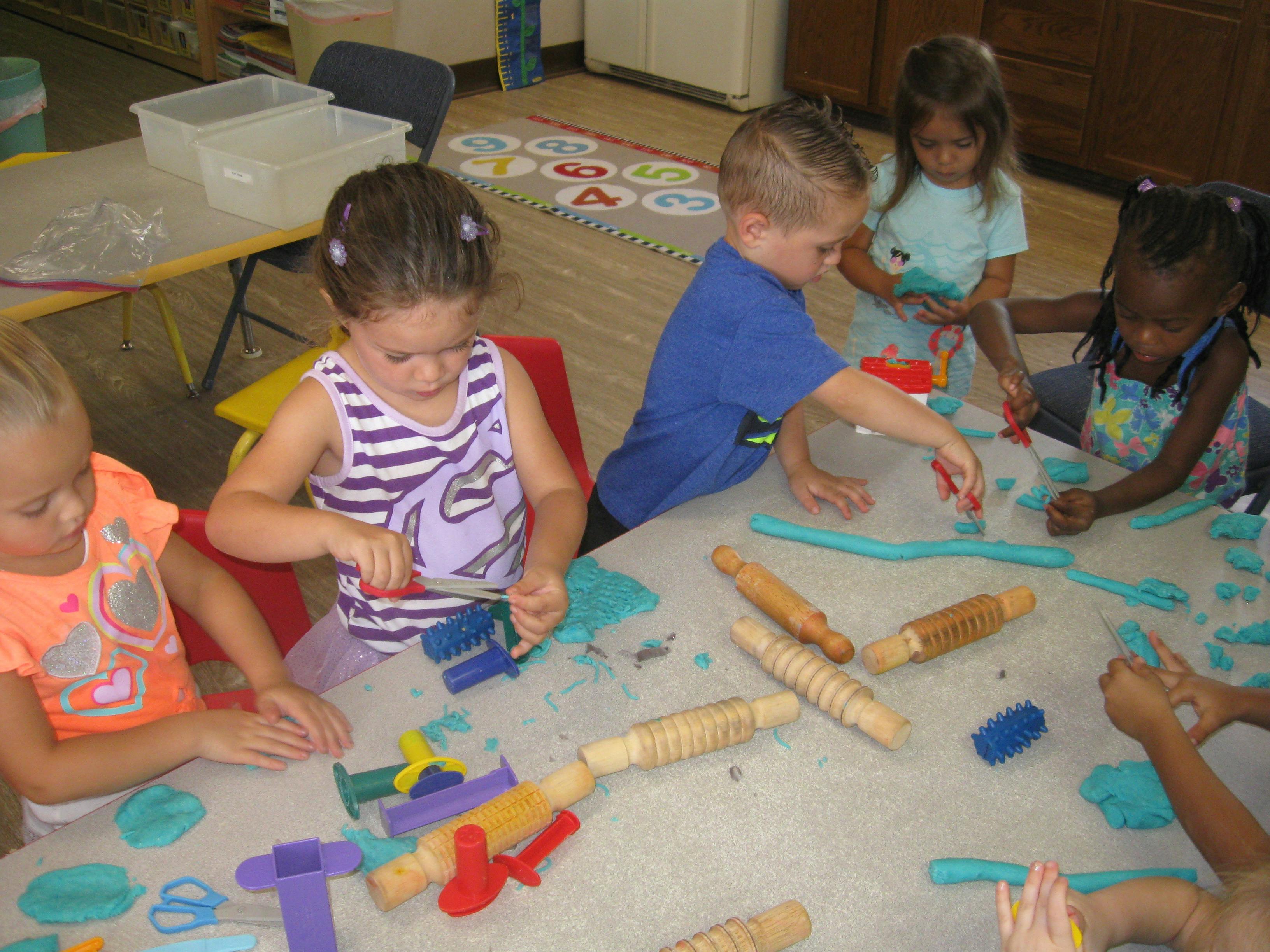 Children playing with modeling clay and rolling pins at a table
