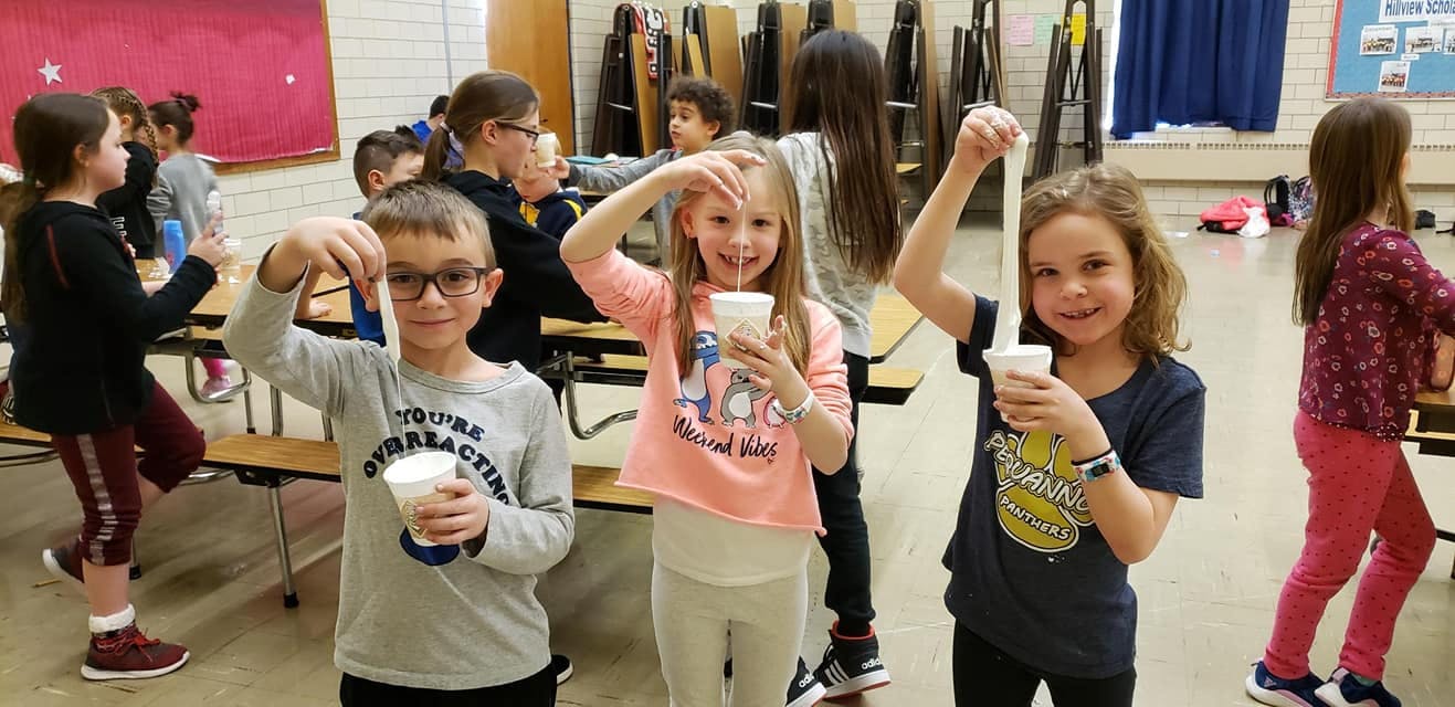 Three children holding cups and stringy material