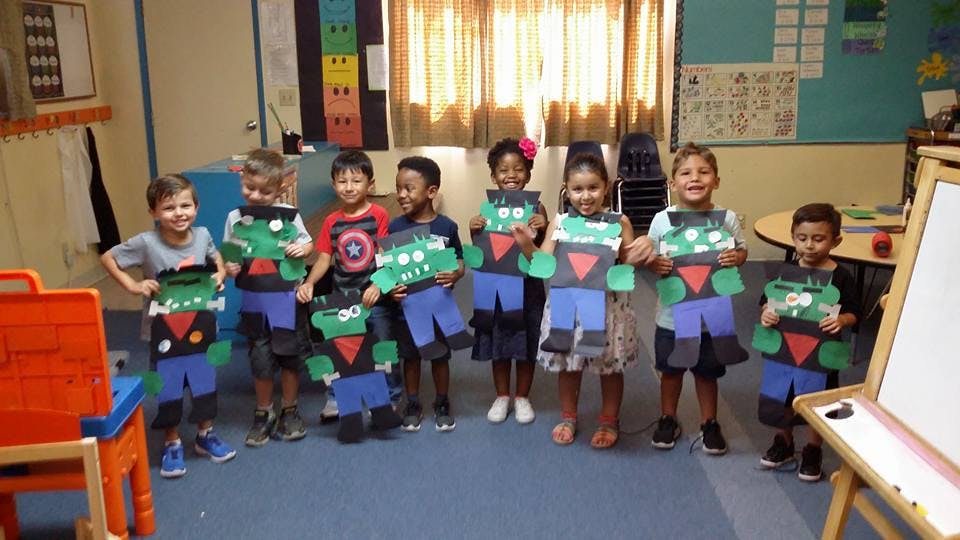 Group of children holding up paper crafts in a classroom