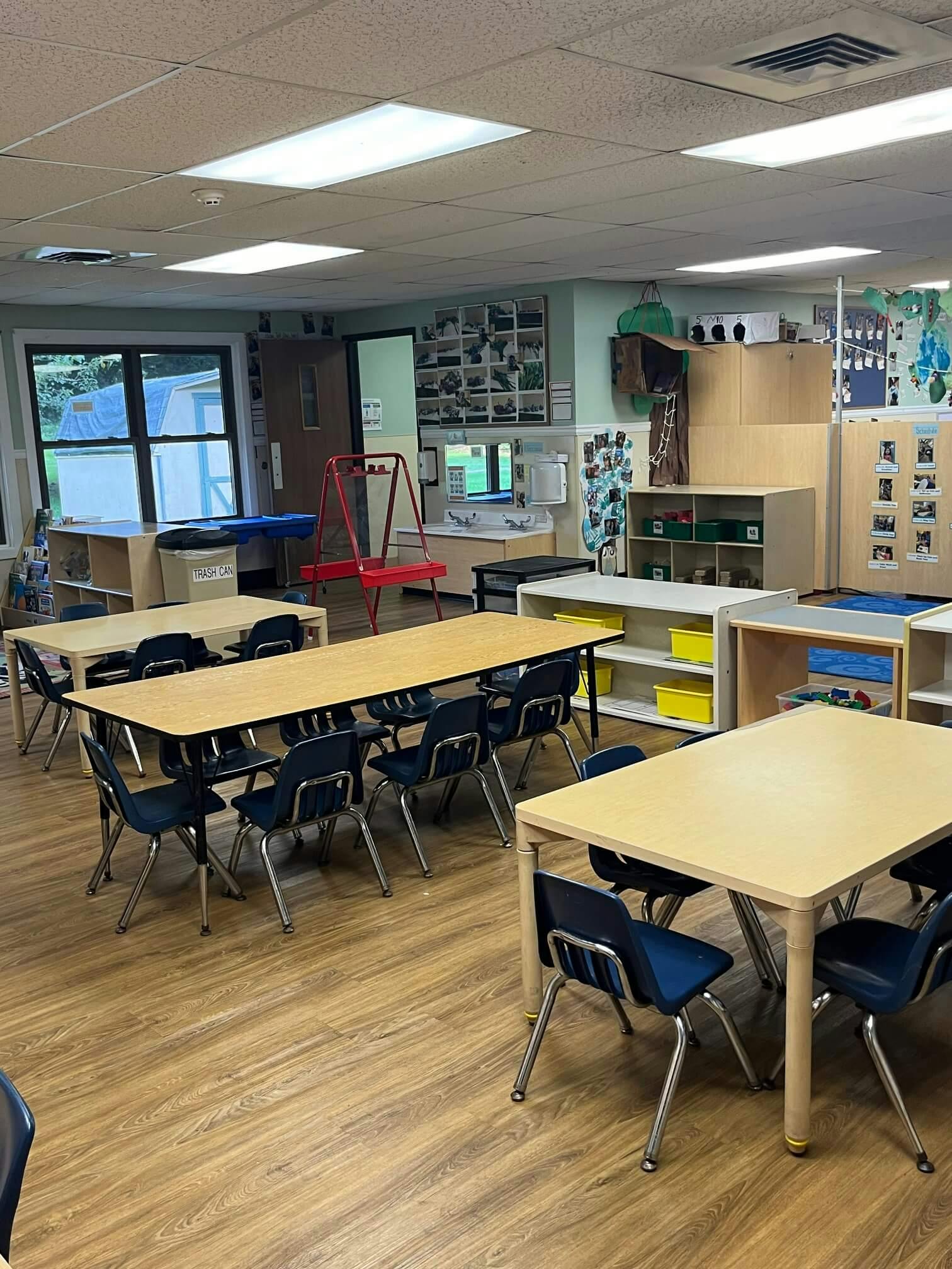 An empty classroom with tables and chairs, and a window overlooking outside