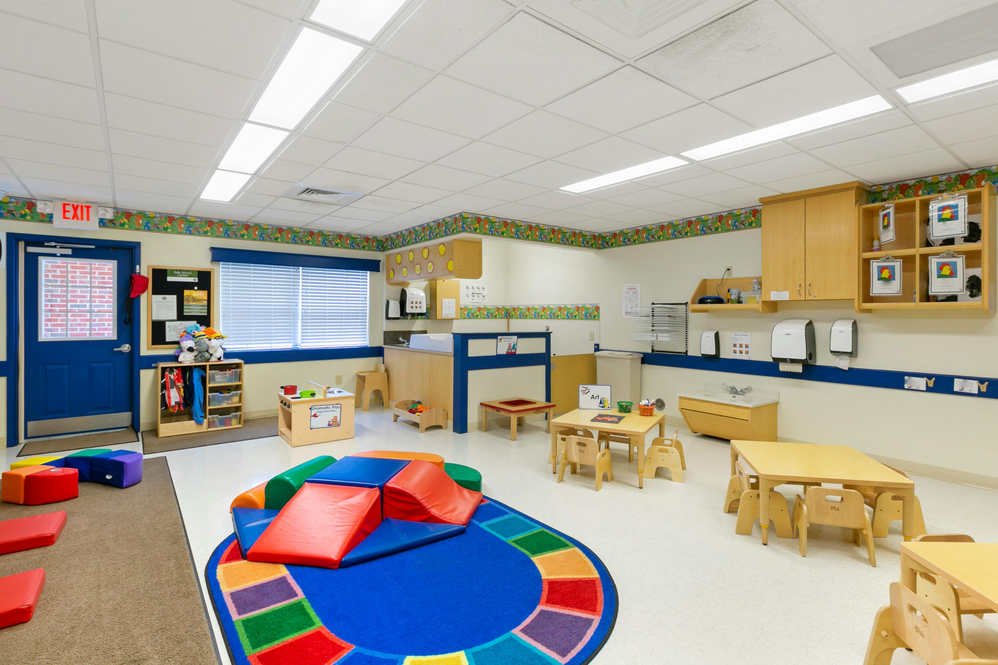 An empty early childhood classroom with play mats, small tables, and a changing station