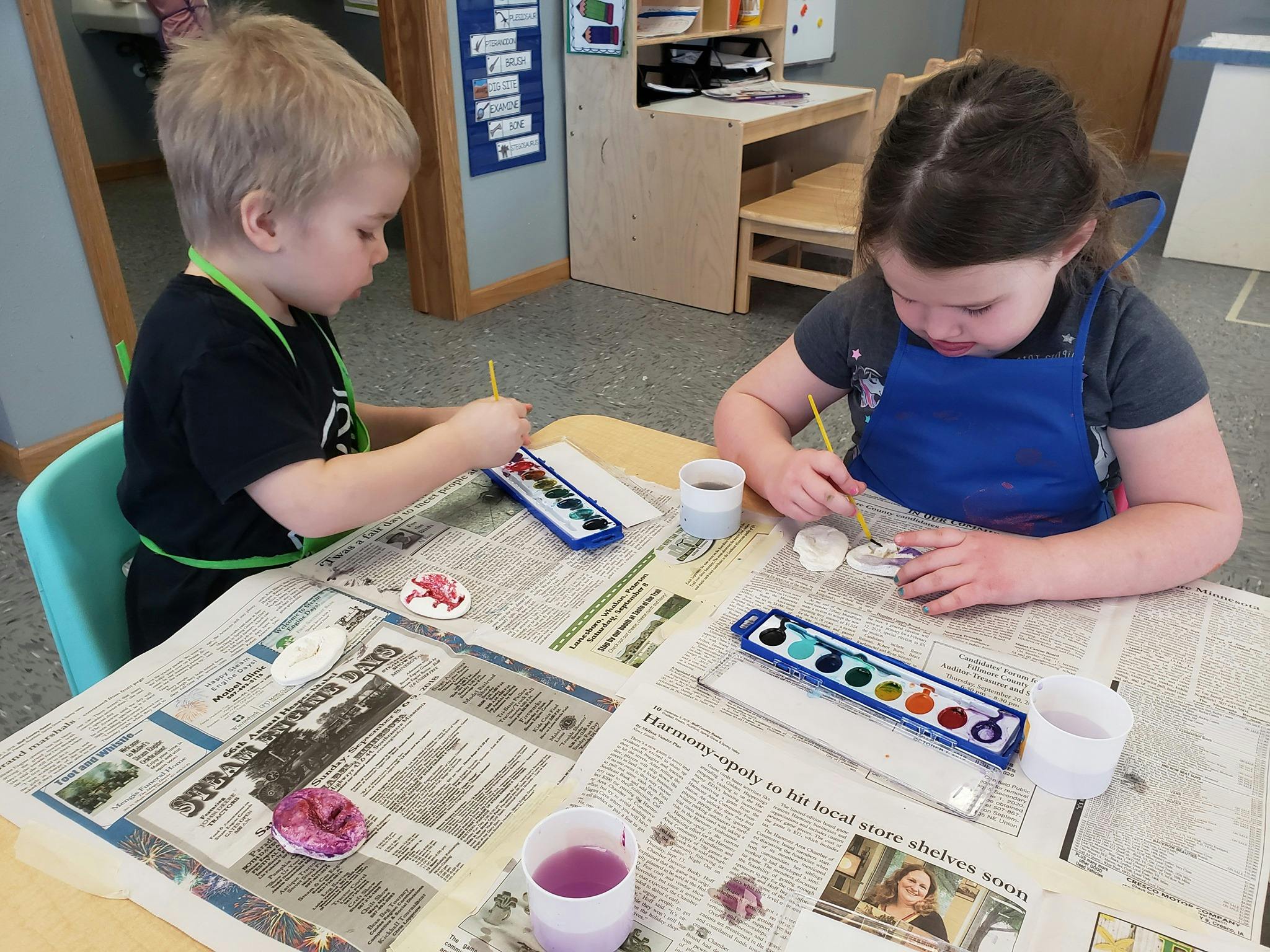 Two children painting at a table in a classroom