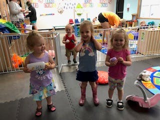 Three children standing in a room, one child in background
