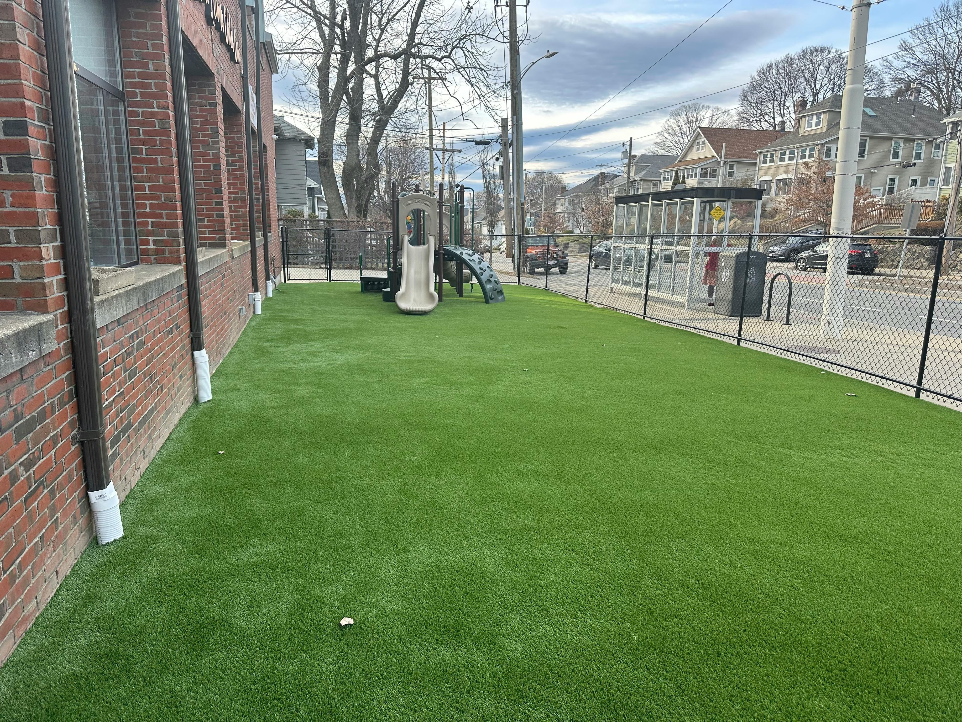 Artificial turf playground next to a brick building and street