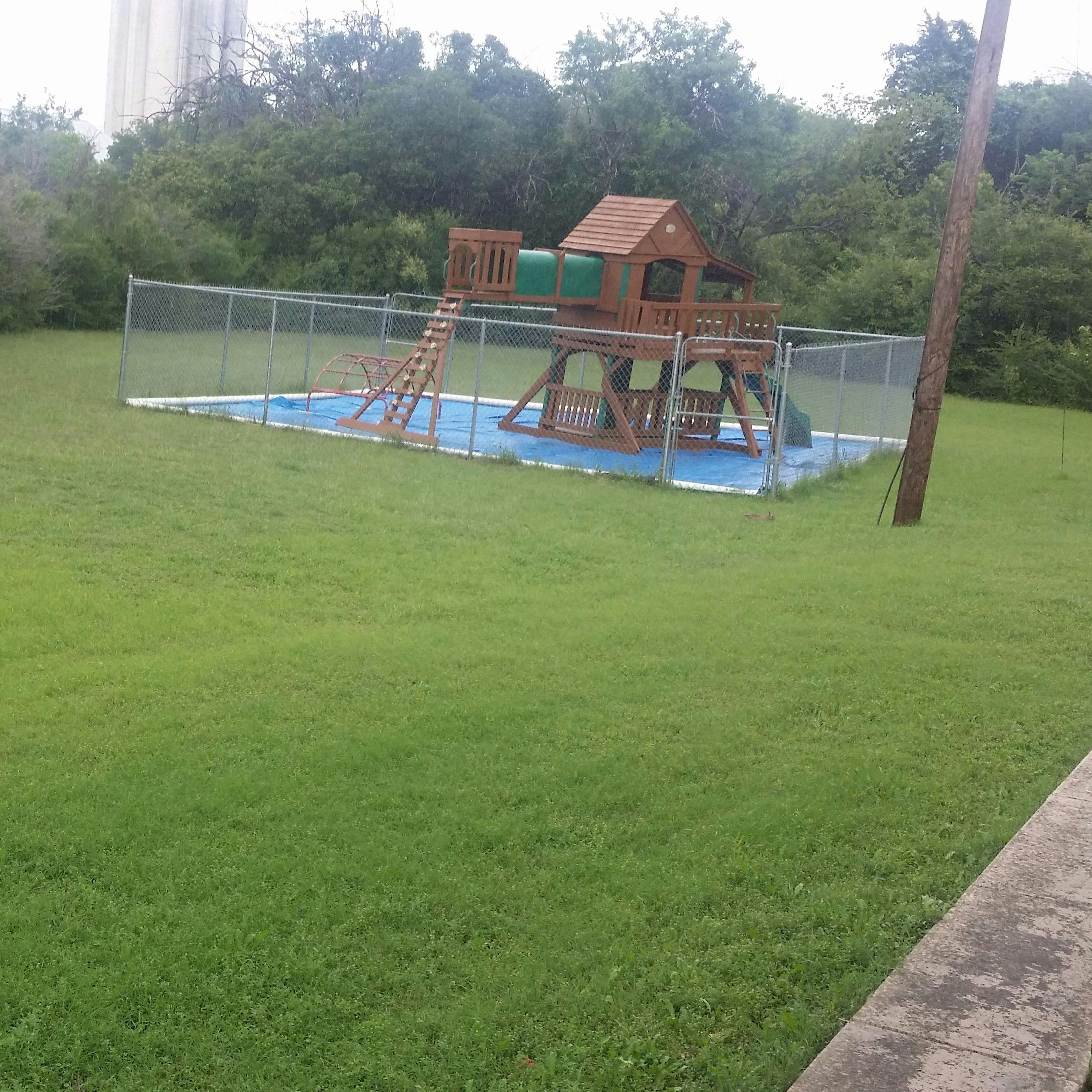 Wooden playground set with a blue mat inside a fenced area
