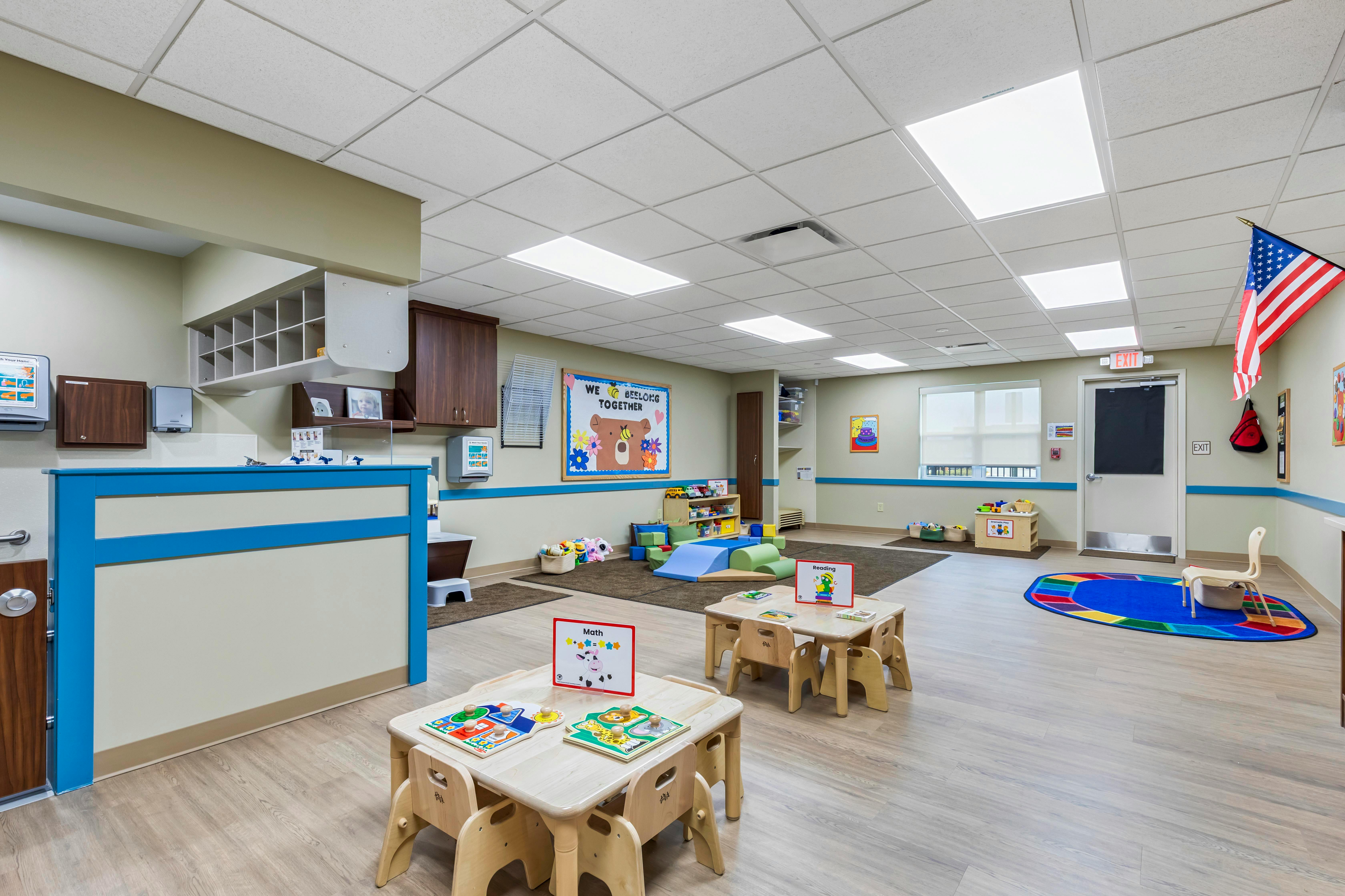 Classroom with small tables and chairs, play mats, and learning posters