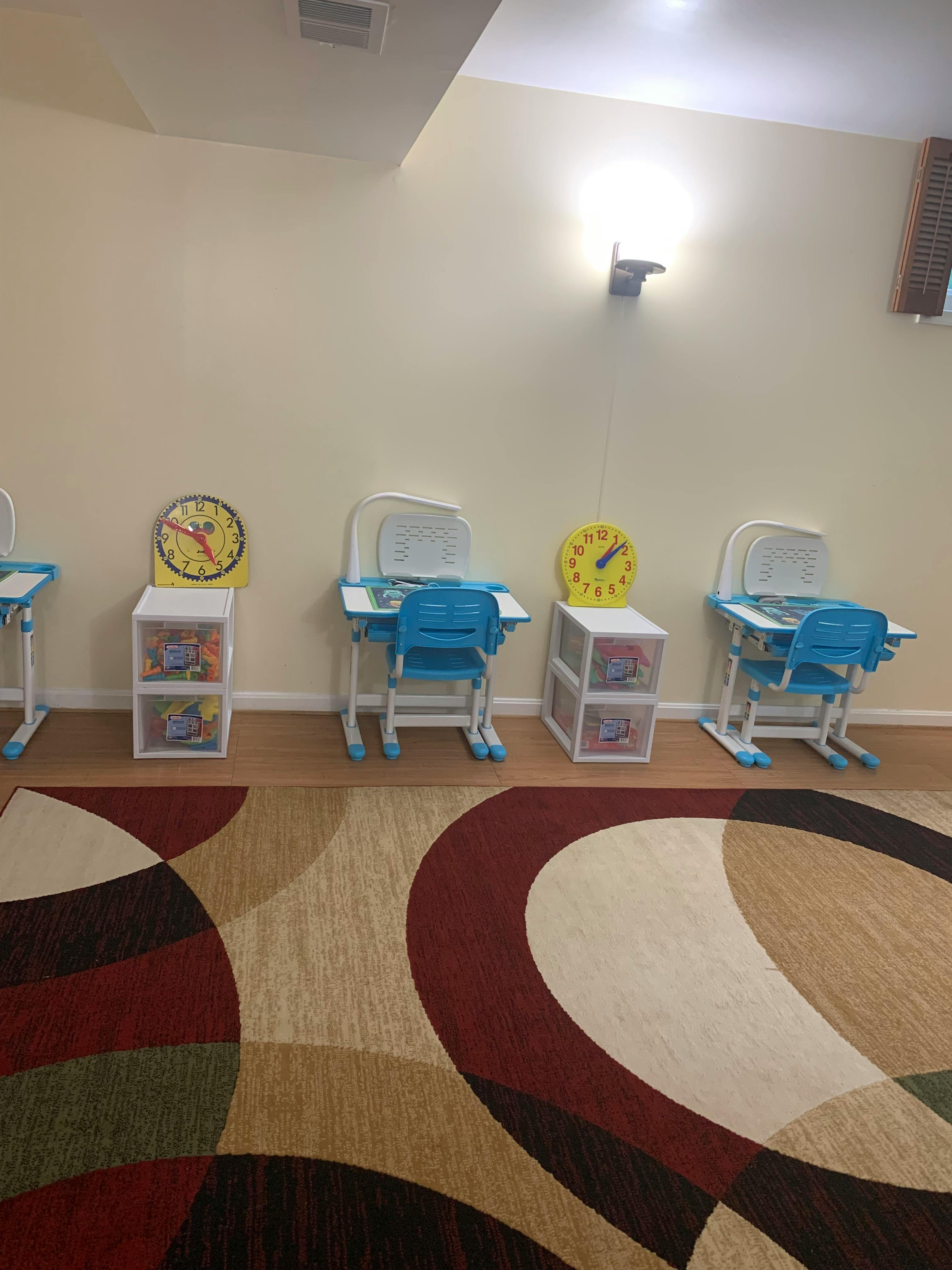 Three blue child-sized desks and chairs with storage units and clocks
