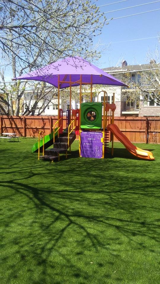 Playground with purple shade canopy, slides, and stairs on green turf
