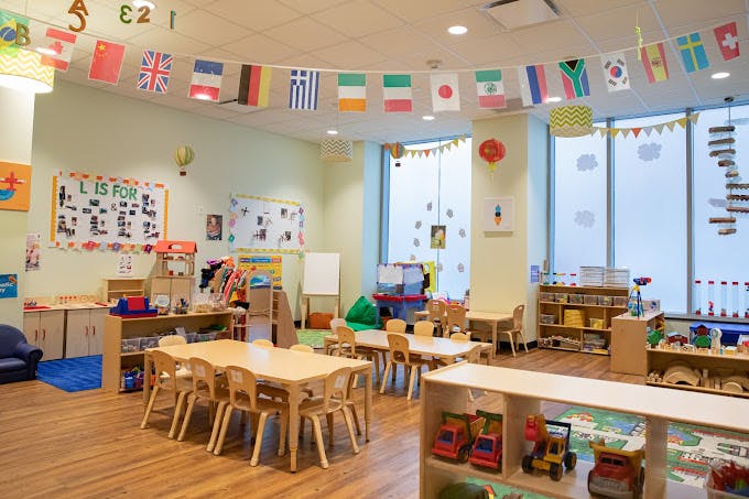 Colorful classroom with small tables and chairs, shelves with toys, and flags hanging