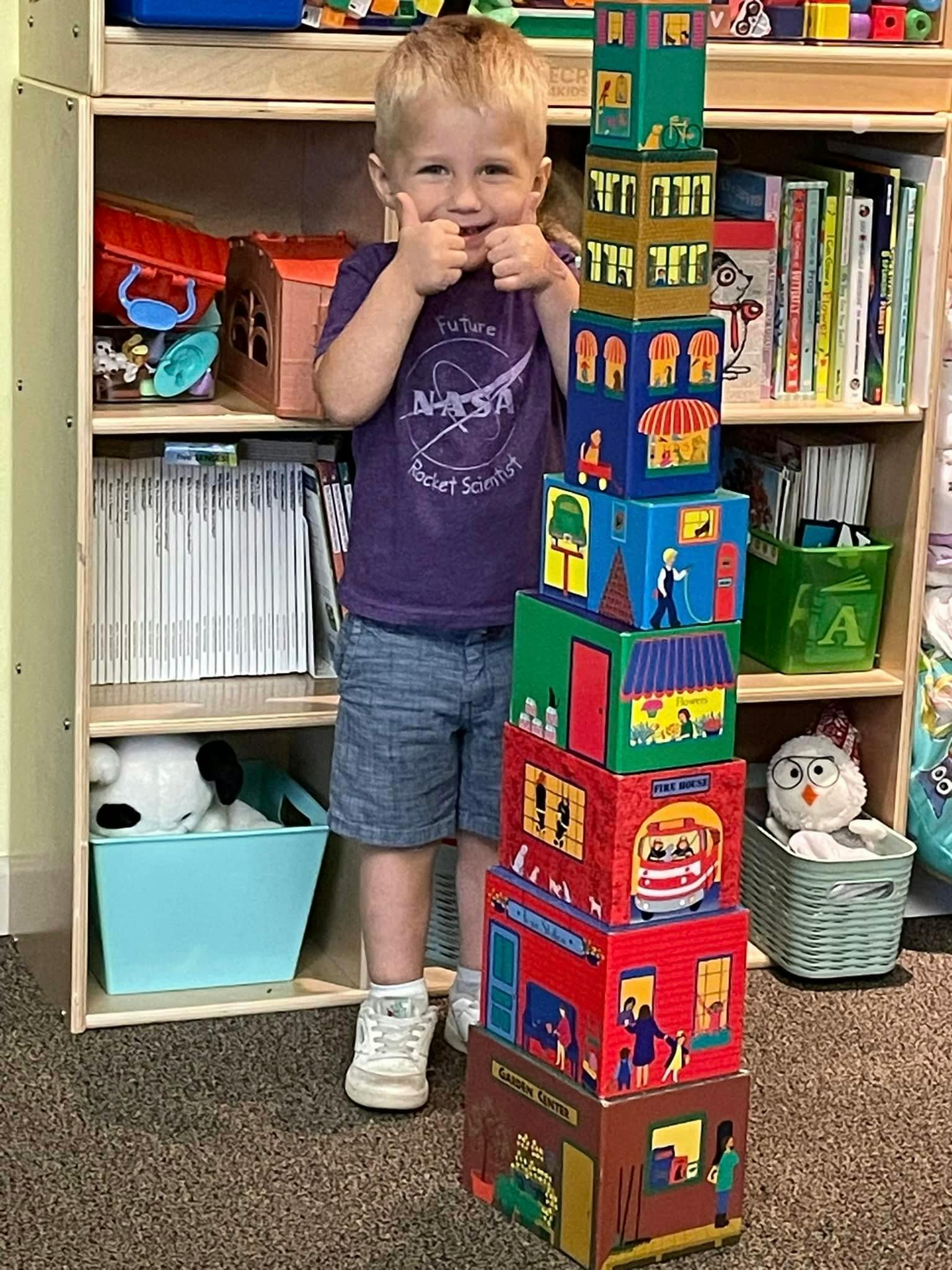 Child giving two thumbs up next to a tall stack of colorful blocks