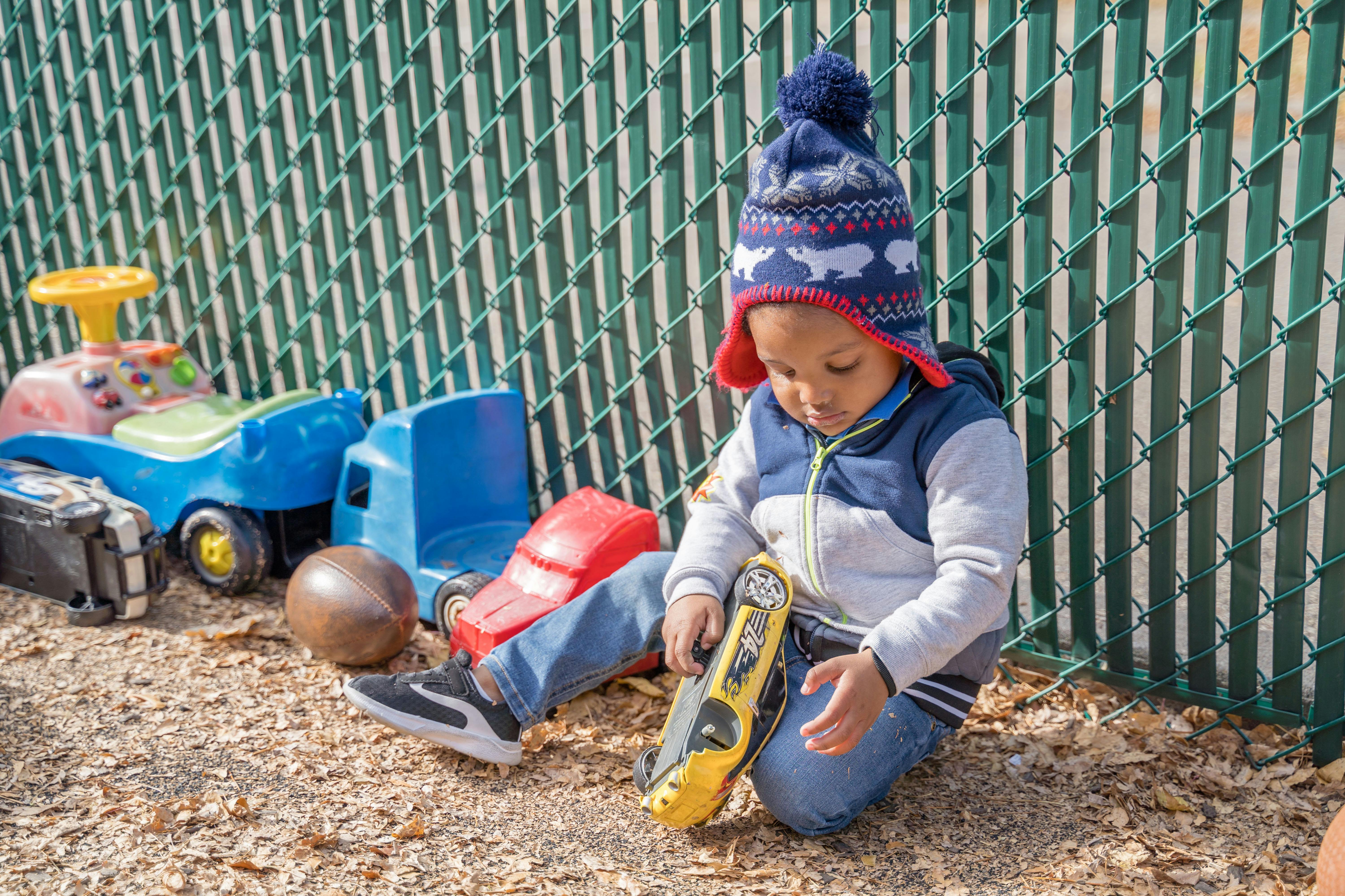 Child in a knit hat playing with a toy car on the ground