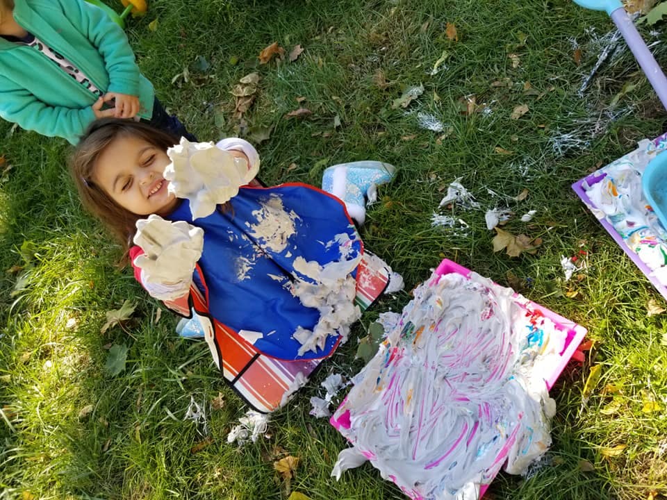 Child with messy hands and bib next to a smashed cake on the grass