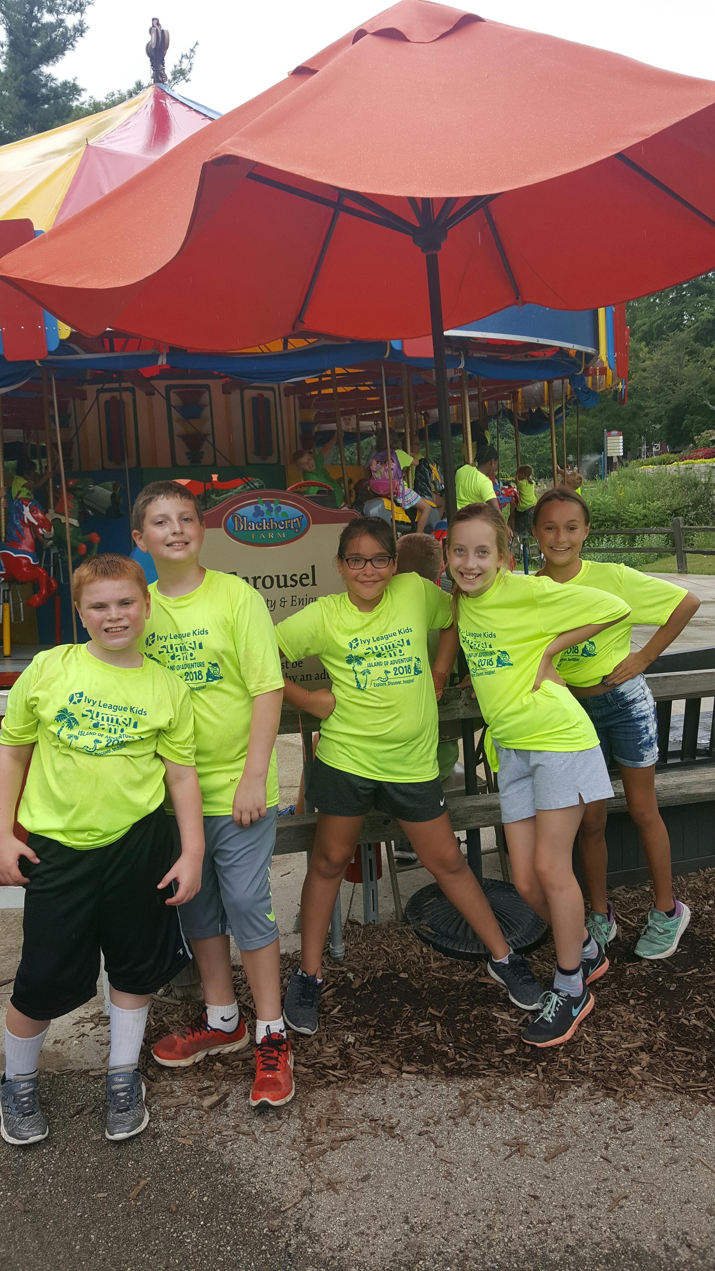 Five children and one teen posing in front of a carousel