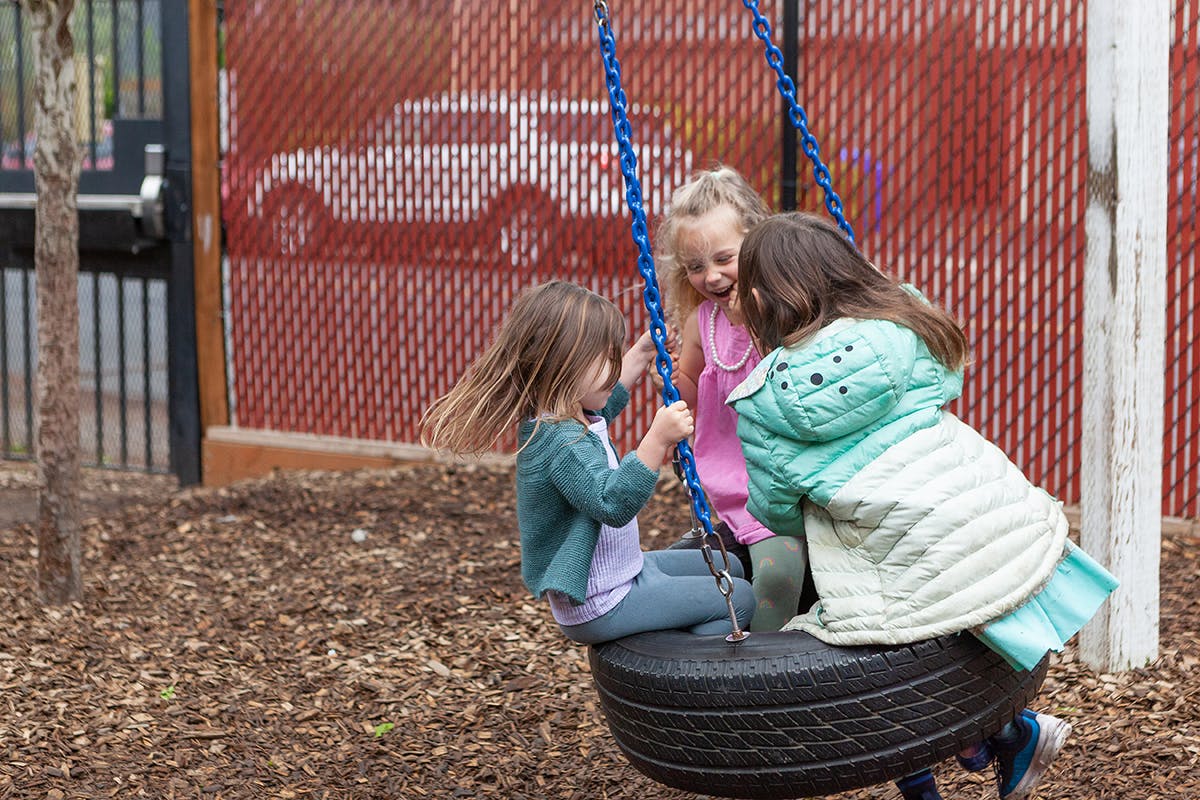 Three children playing on a tire swing