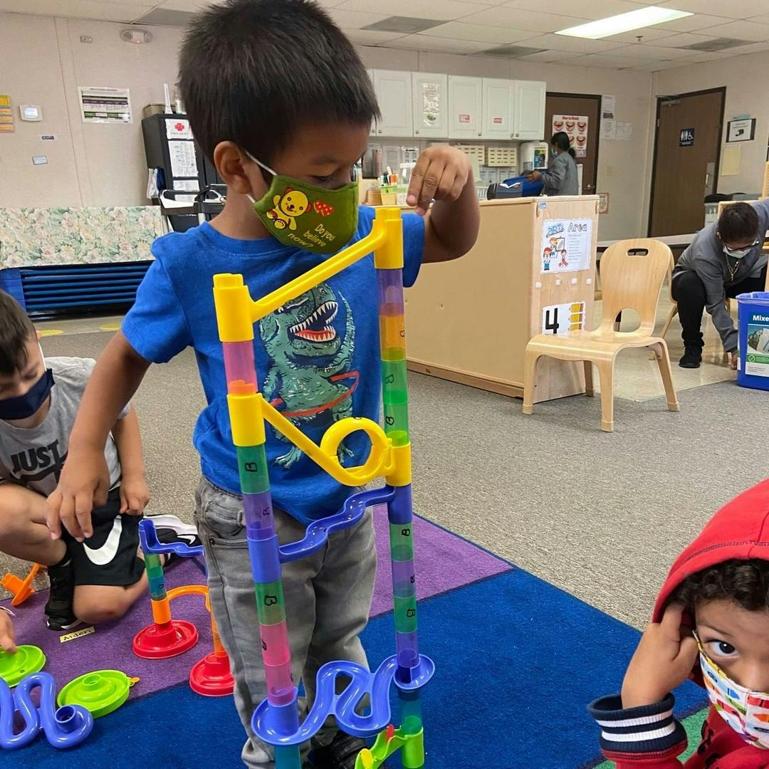 Child in a mask playing with a colorful marble run toy