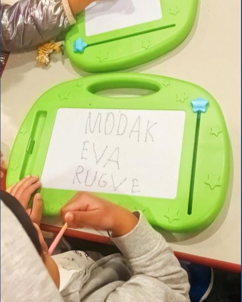 Child writing the words MODAK EVA RUGVE on a magnetic drawing board