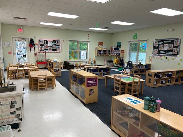 Classroom with small wooden tables and chairs, storage units, and a sink area