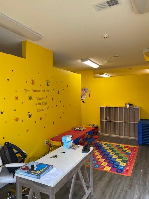 Classroom with yellow walls, tables, and a colorful rug