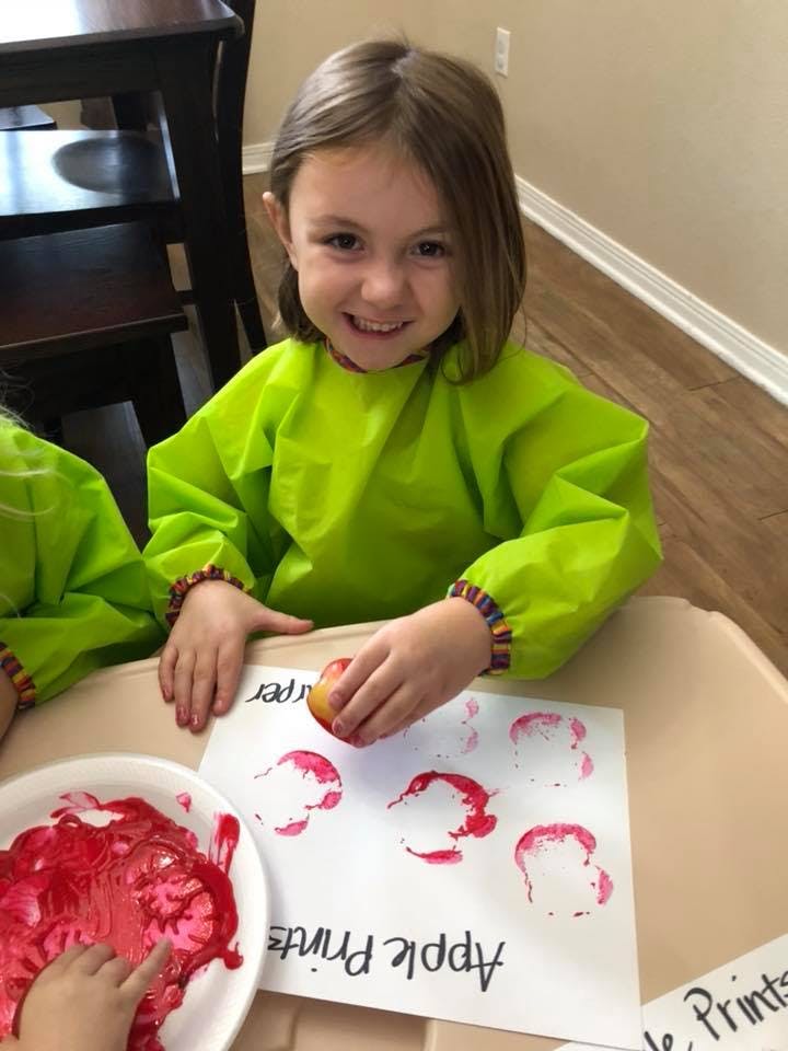 Child in a smock making apple prints on paper