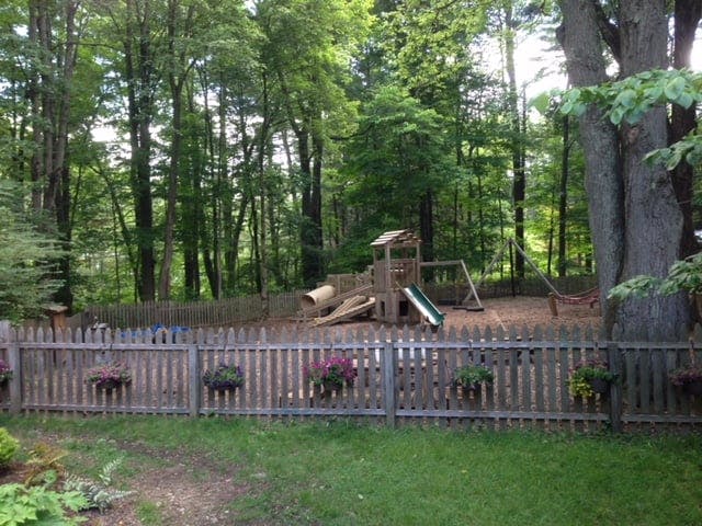 Wooden fence in front of a playground with slides and swings