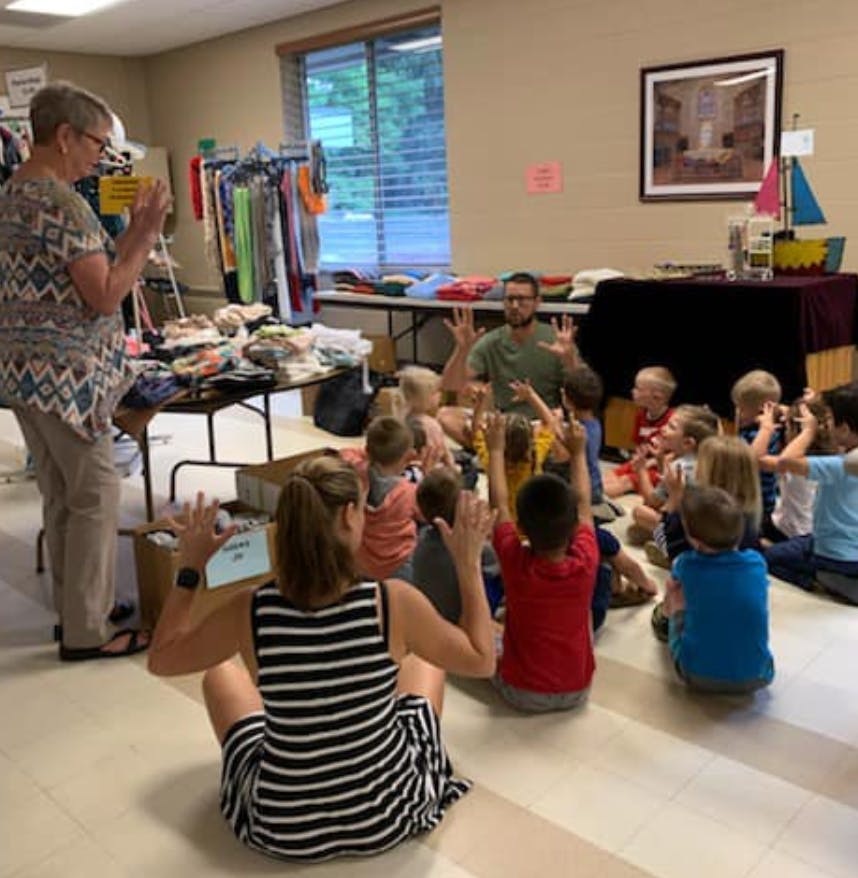 Adults and children sitting on the floor with hands raised