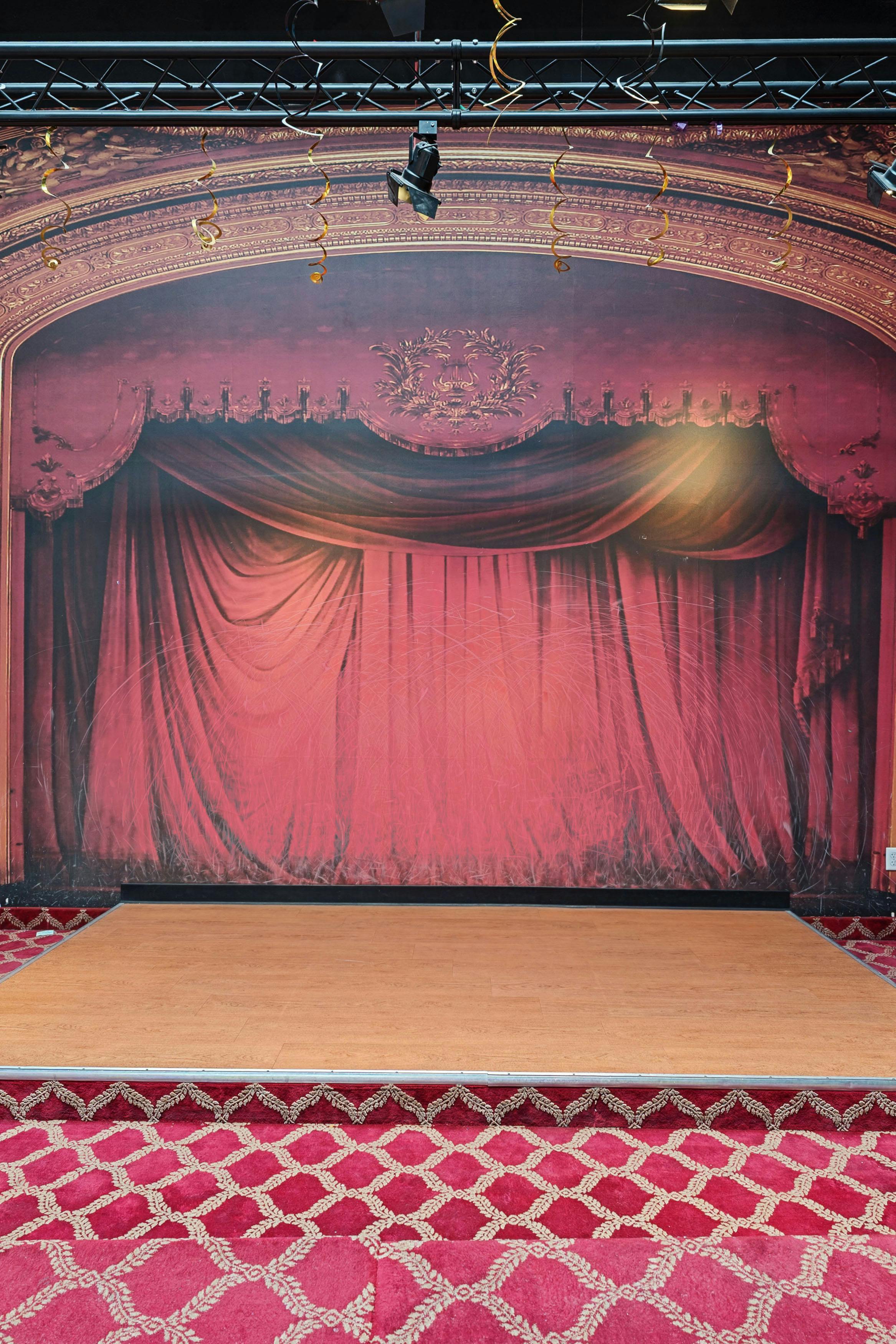 Stage set with red curtains and a wooden floor, with red patterned carpet steps