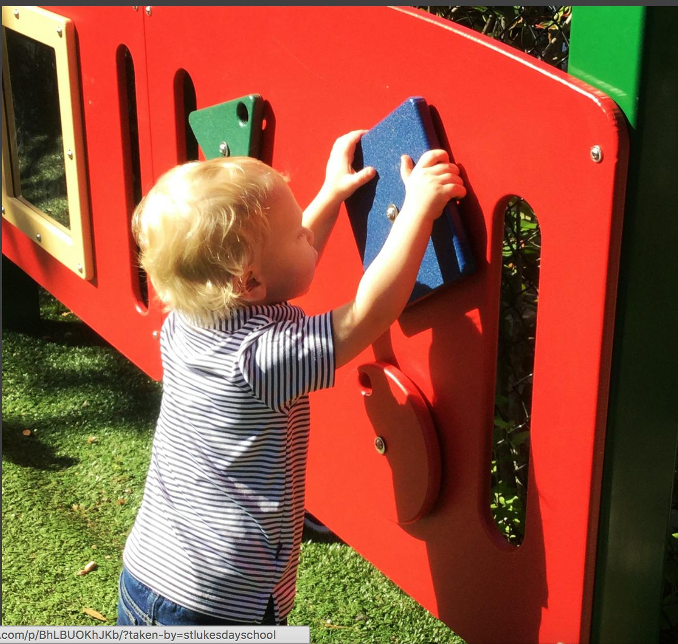 Child playing with a blue block on a red playground structure