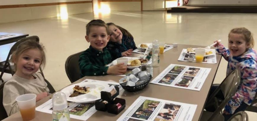 Four children sitting at a table with plates of food and drinks
