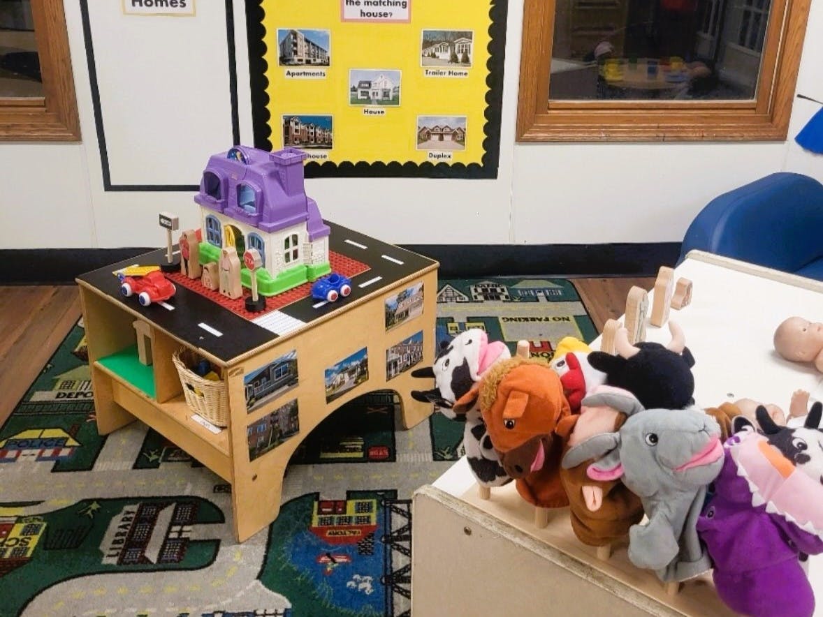 Toy house and cars on a play table with puppet toys nearby