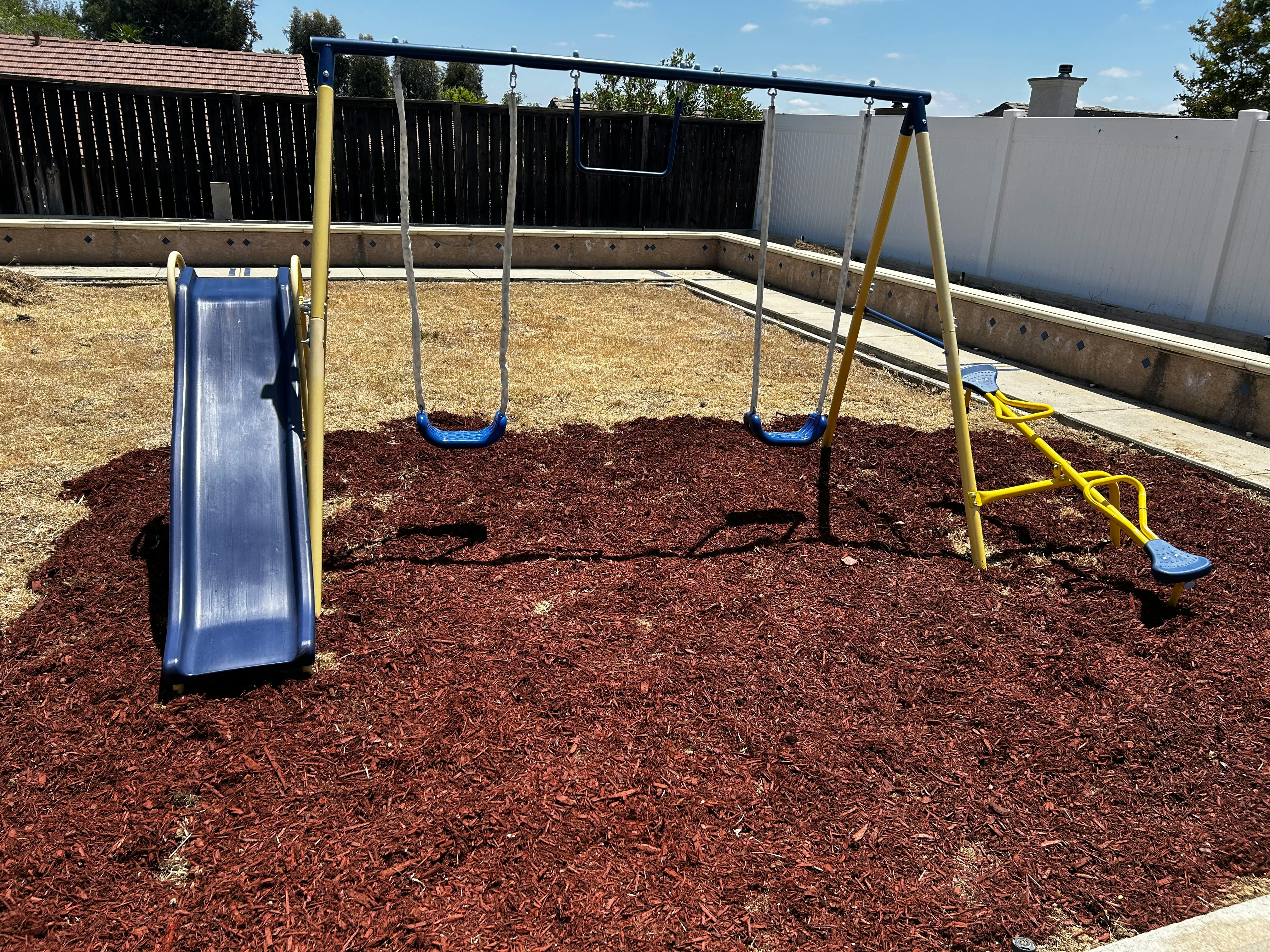 Playground with slide, swings, and seesaw on wood chips