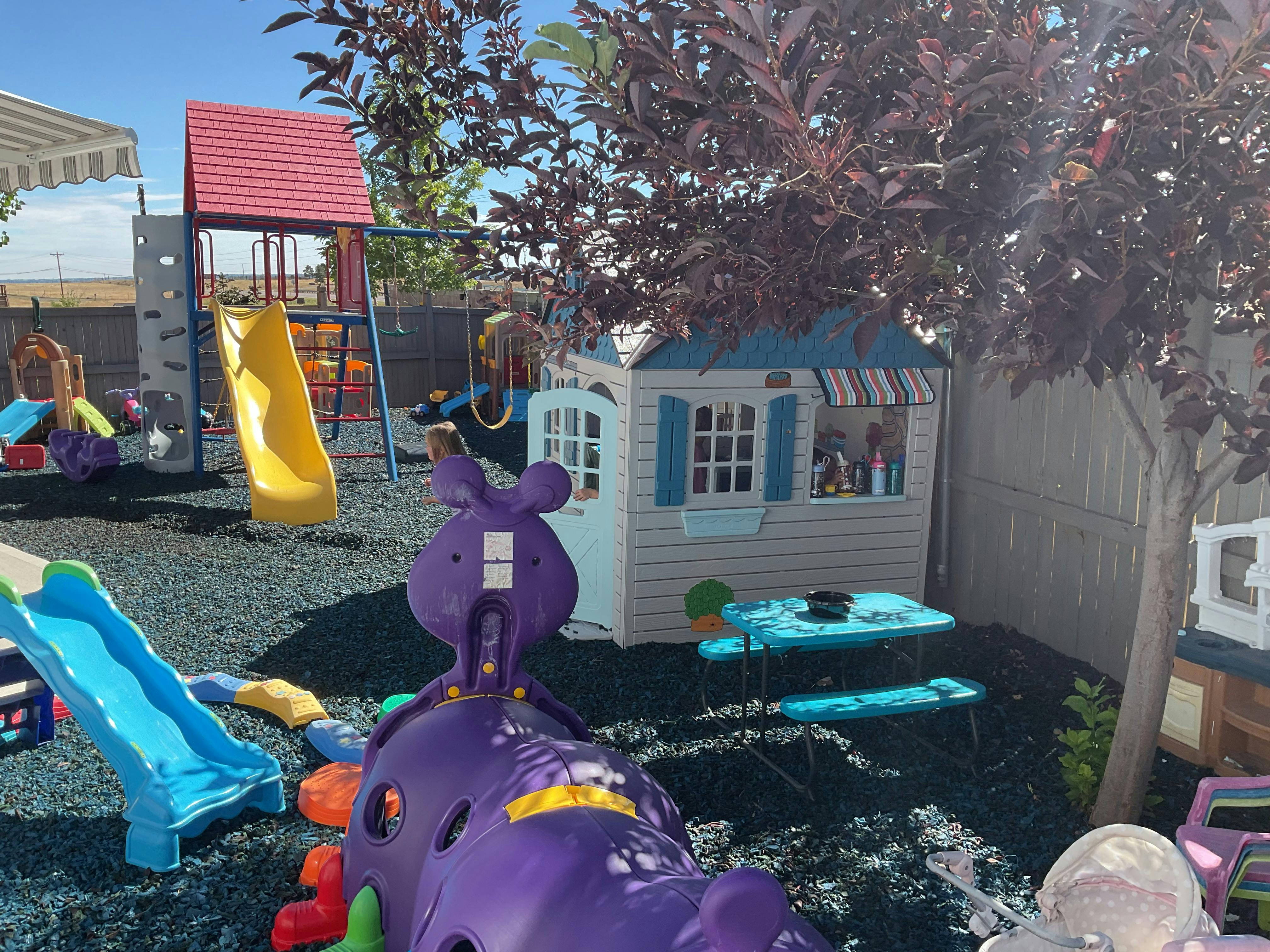 Child playing in a backyard playground with a playhouse and slides