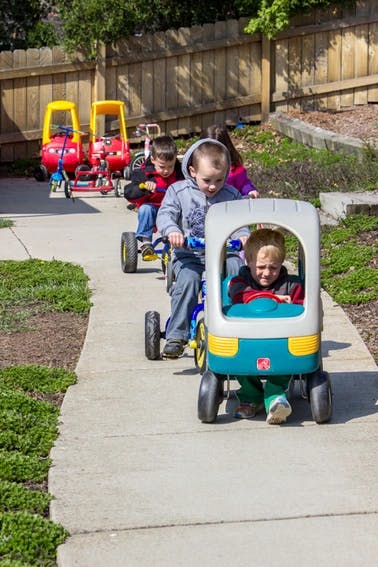 Children riding toy vehicles on a sidewalk