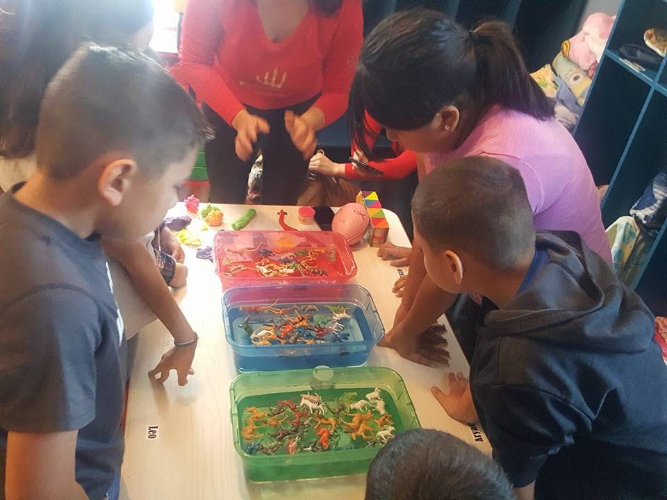 Adults and children gathered around a table with colorful bins of sensory bins