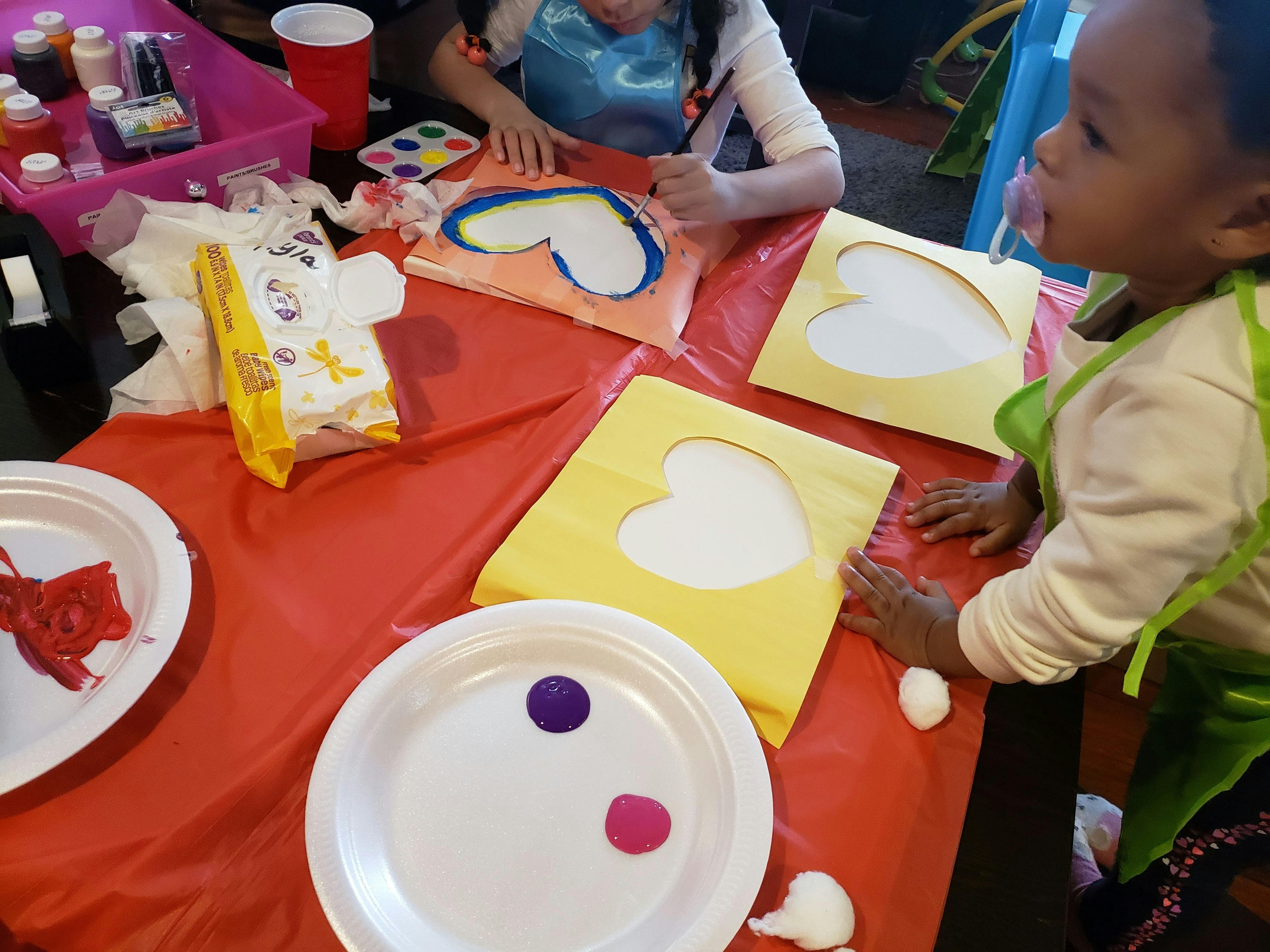 Two children painting heart shapes on paper