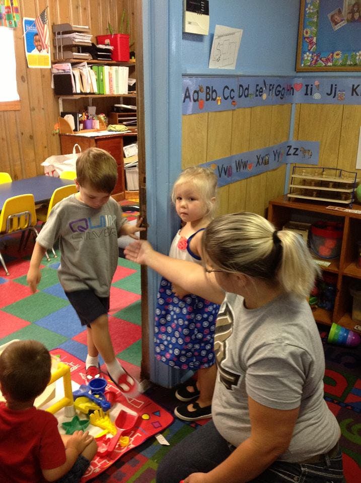 Adult and two children in a classroom, one child playing on the floor