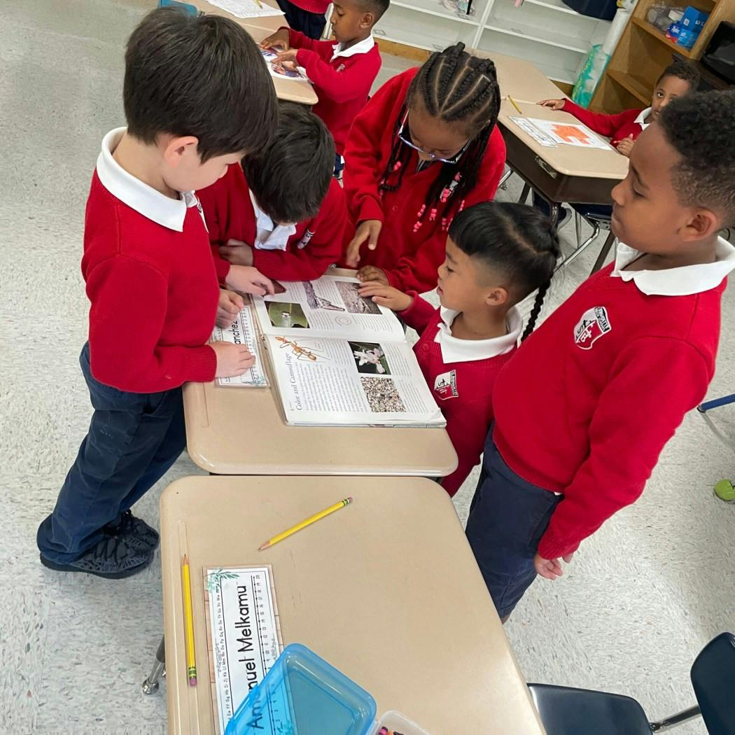 Children looking at a book on a desk in a classroom