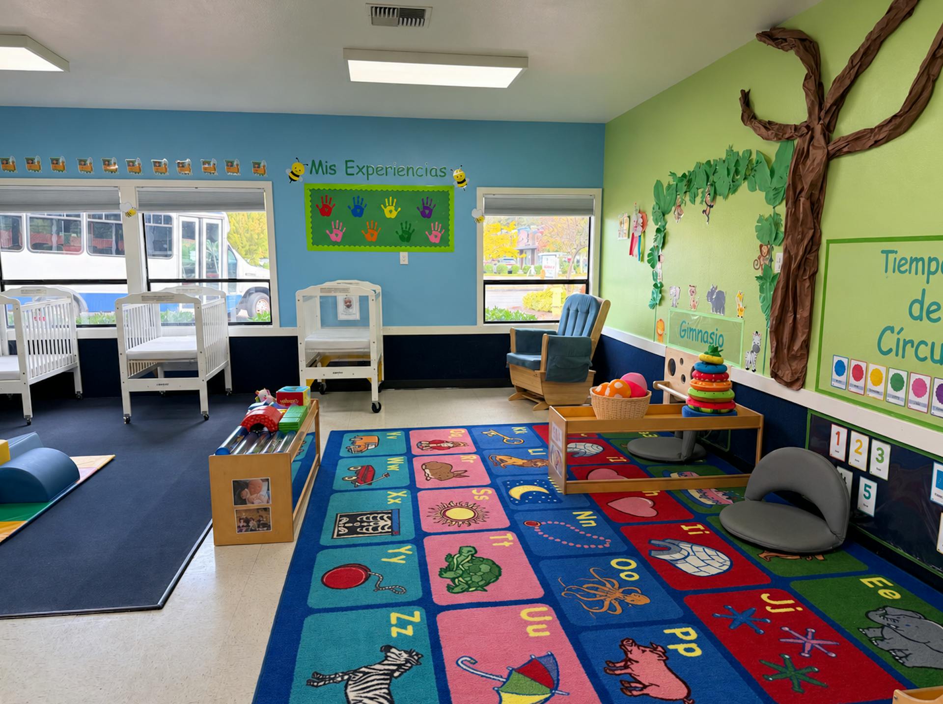 Colorful classroom with play area including cribs and an educational rug