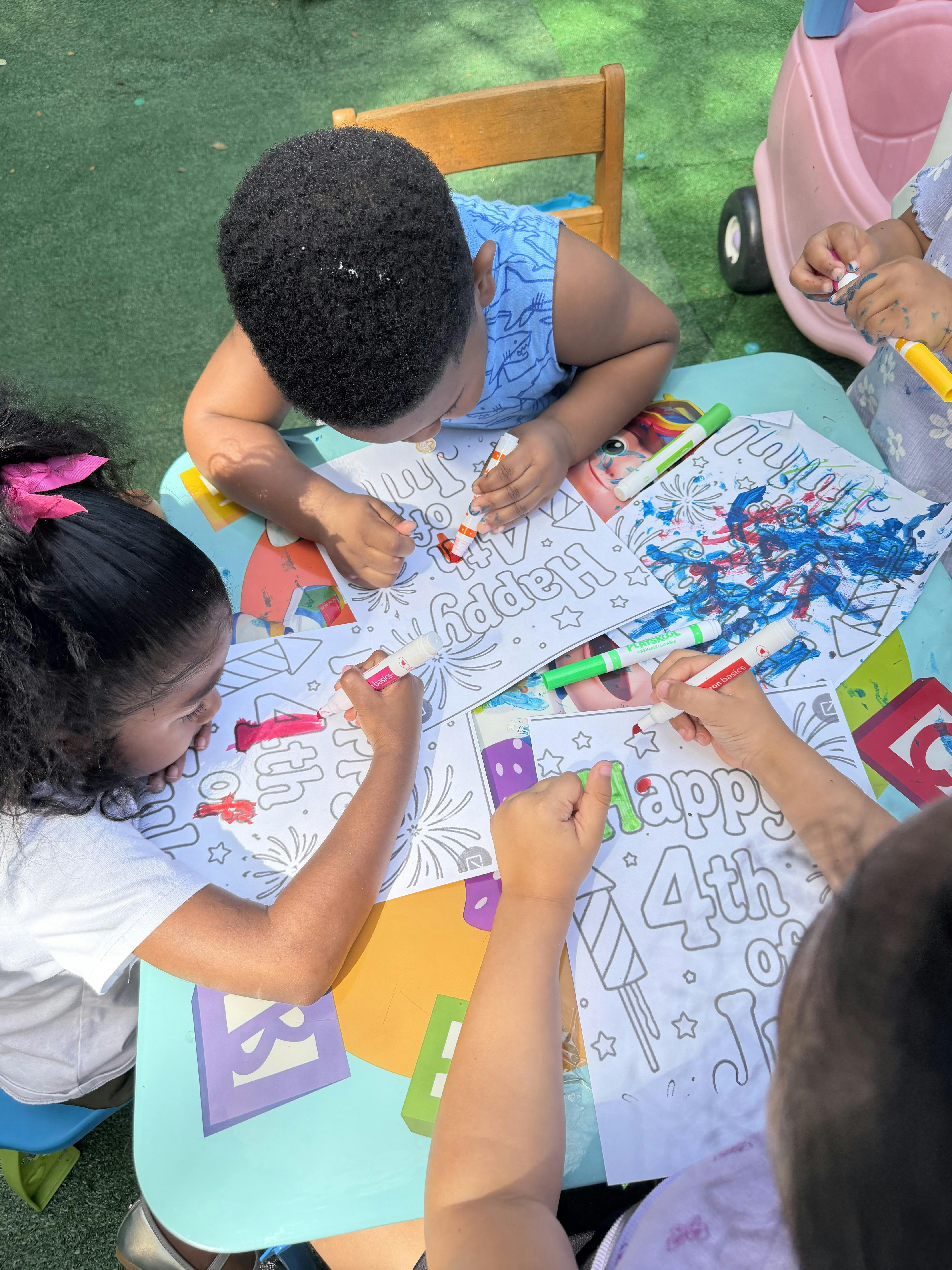 Children coloring Happy 4th of July pages with markers at a table