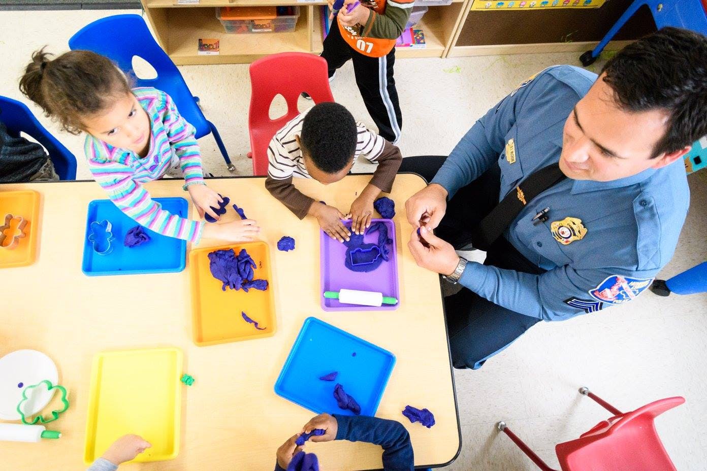 Adult in uniform and children playing with modeling clay at a table