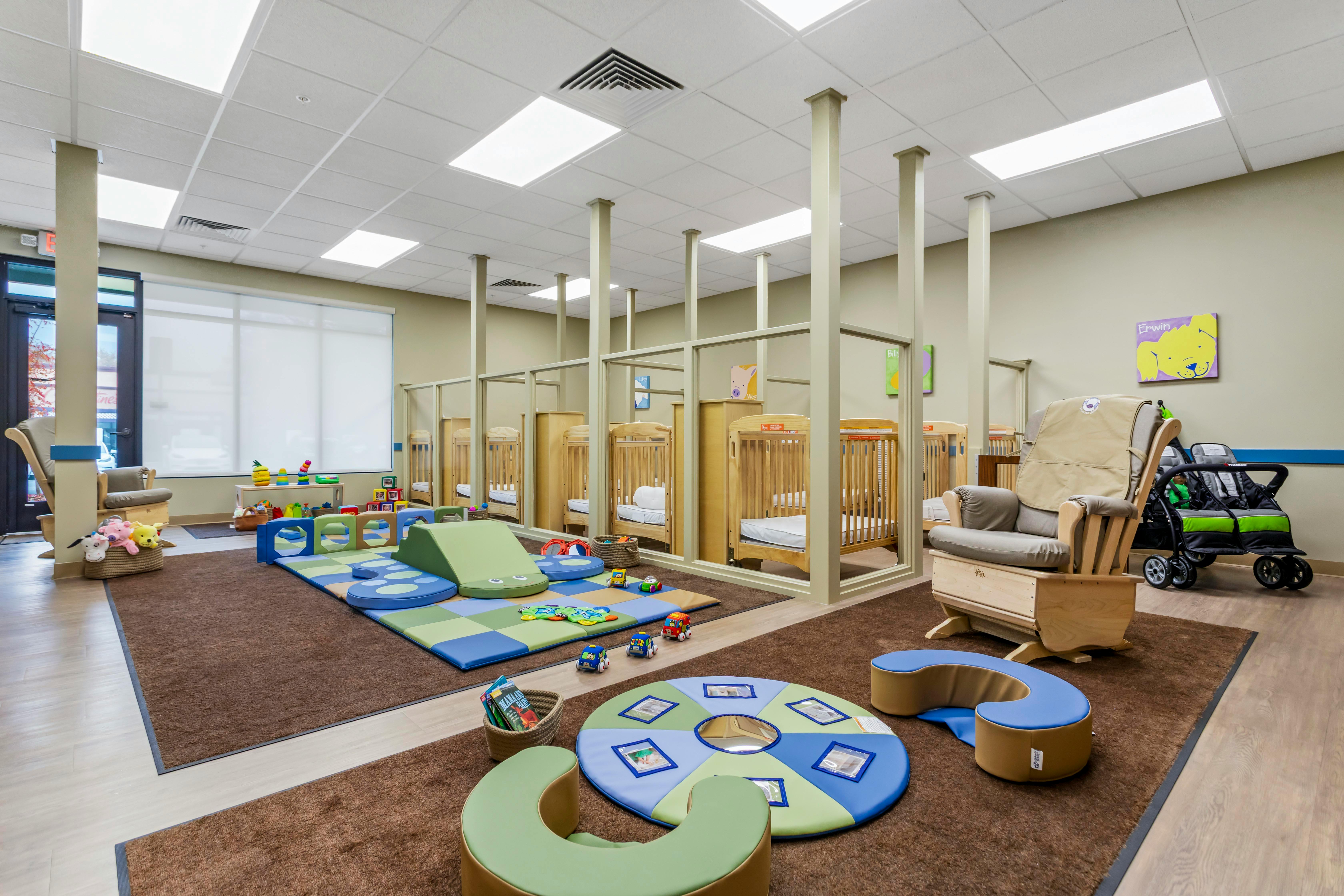 A room with multiple cribs, play mats, and a rocking chair