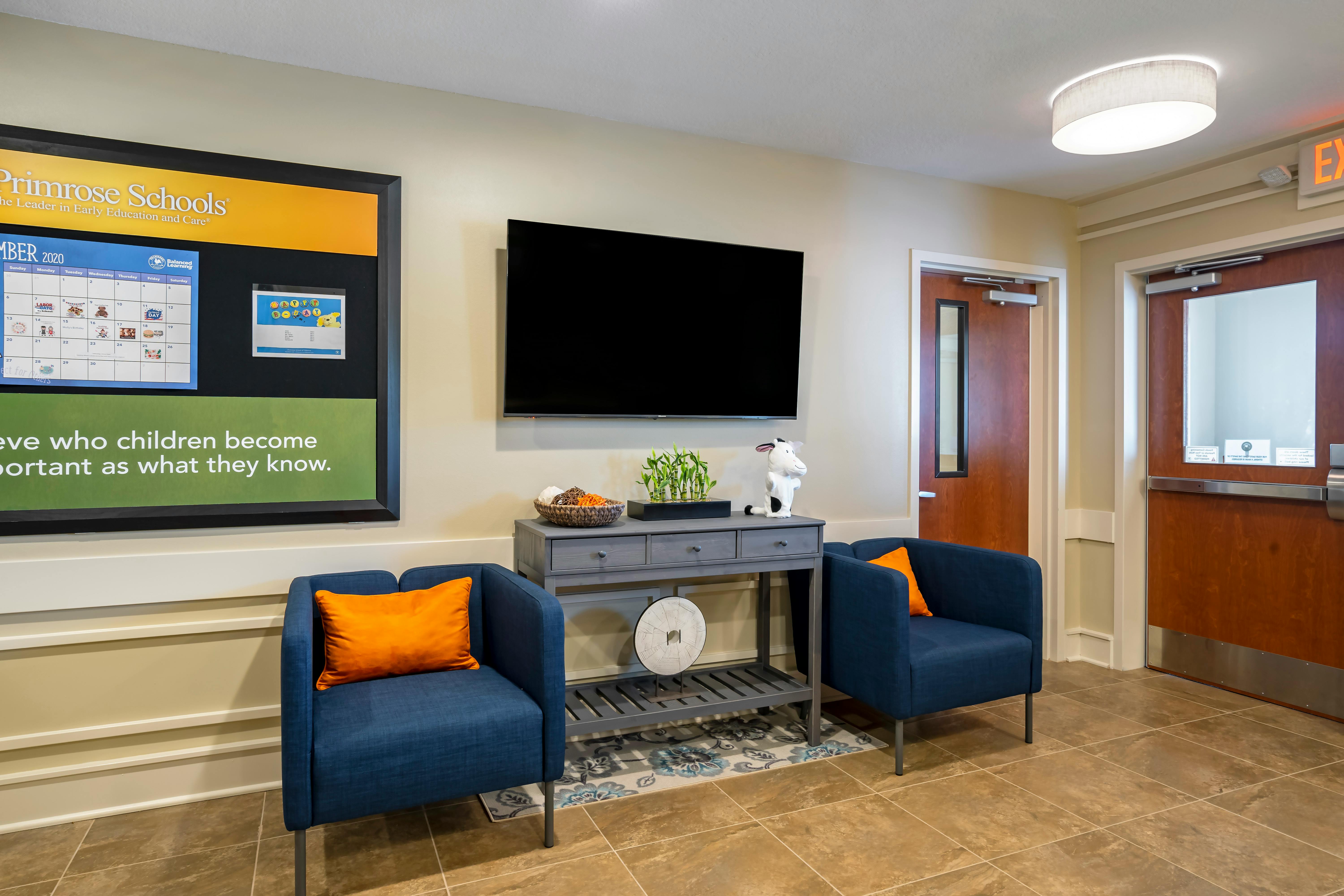 Lobby waiting area with two armchairs, a television, and a Primrose Schools sign