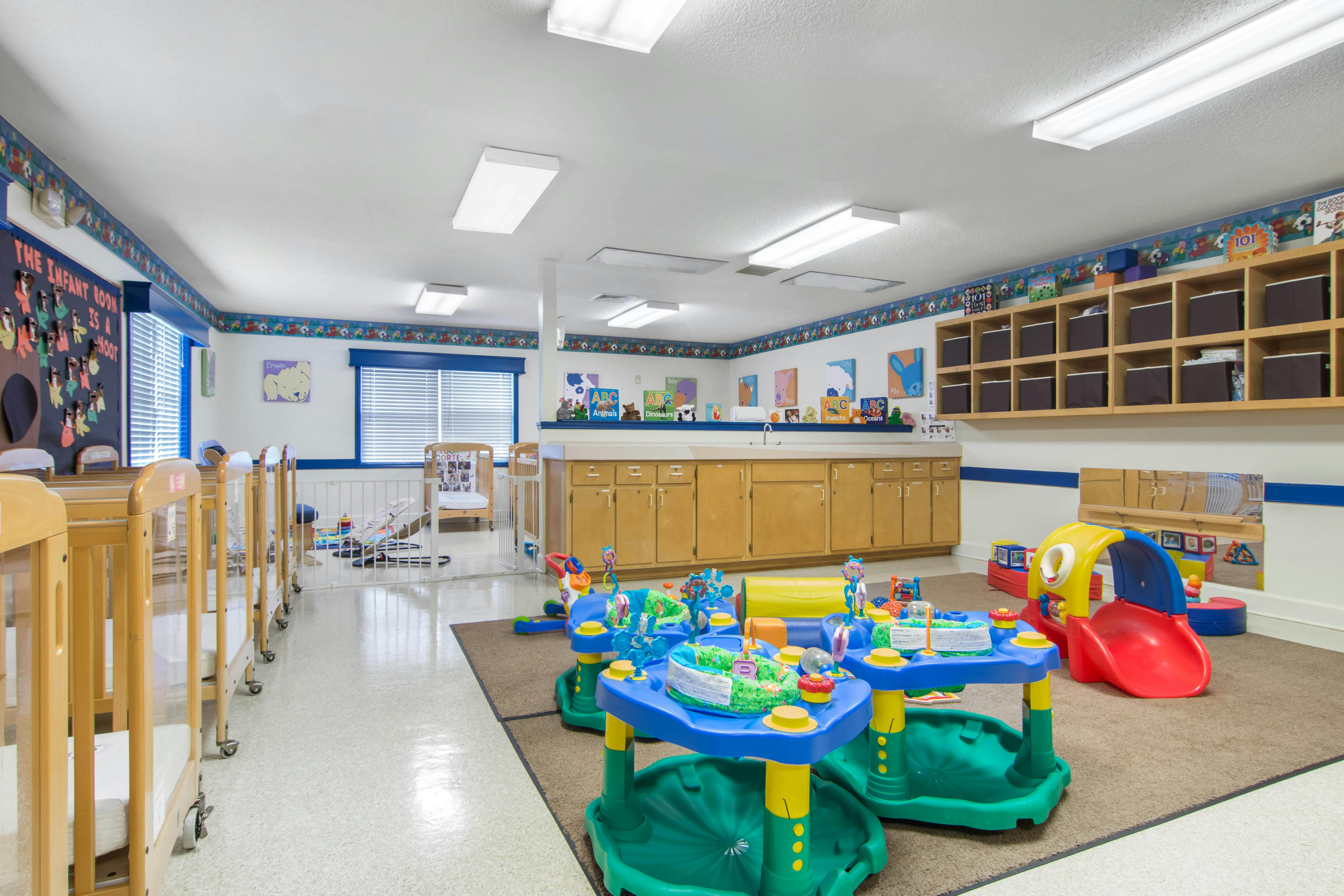 An infant room with multiple cribs, a changing counter, and play mats with toys