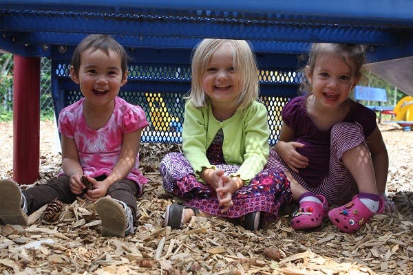 Three children sitting on wood chips under a play structure