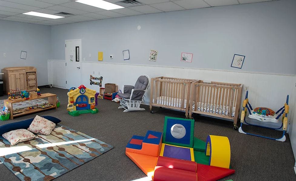 Room with two cribs, a rocking chair, and colorful play equipment