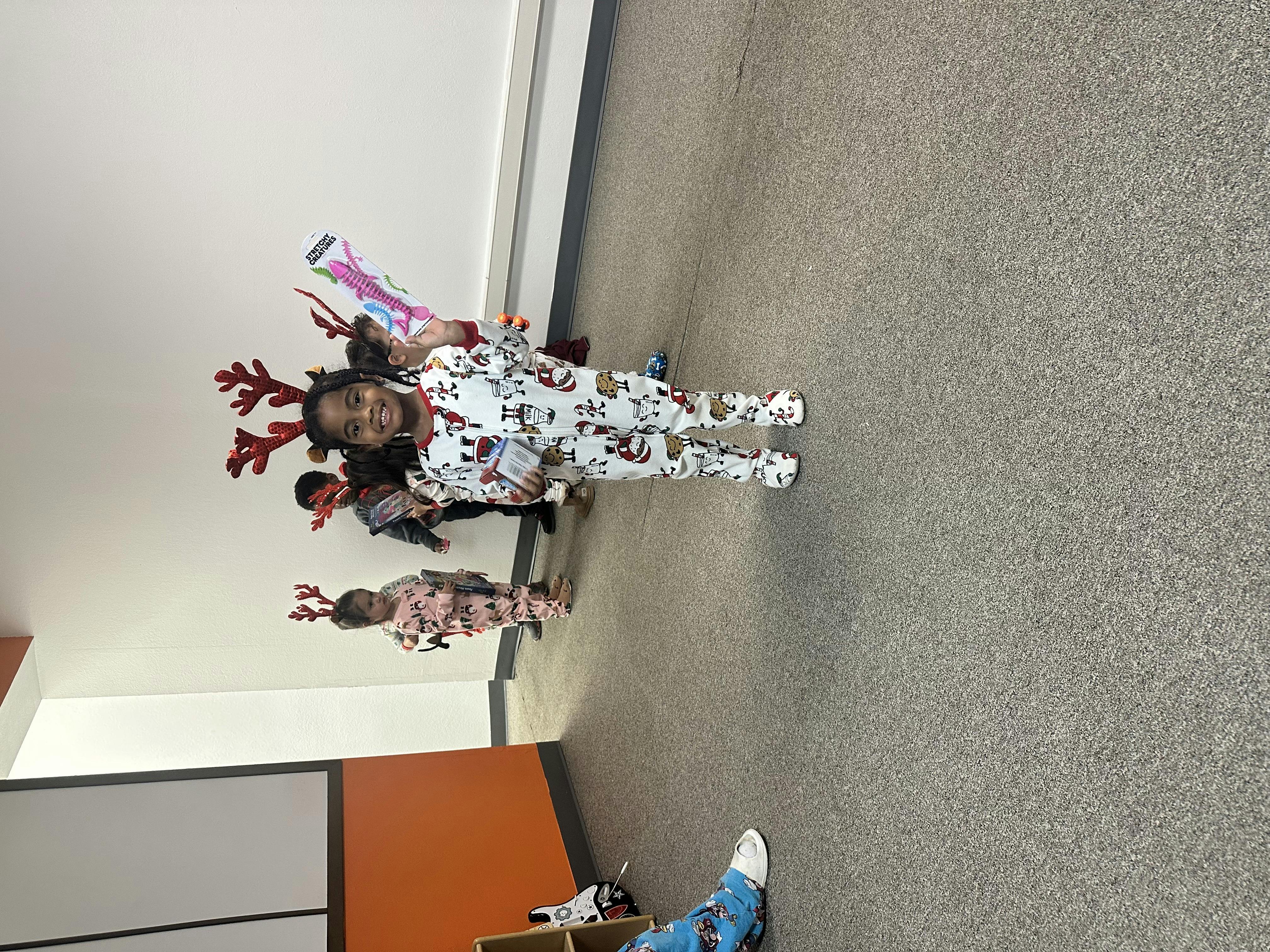 Child in pajamas and reindeer antlers standing with other children