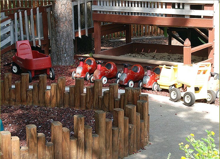Red wagon and ride-on toys next to a sandbox
