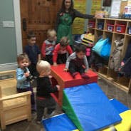 Adult and multiple children in a room with play equipment