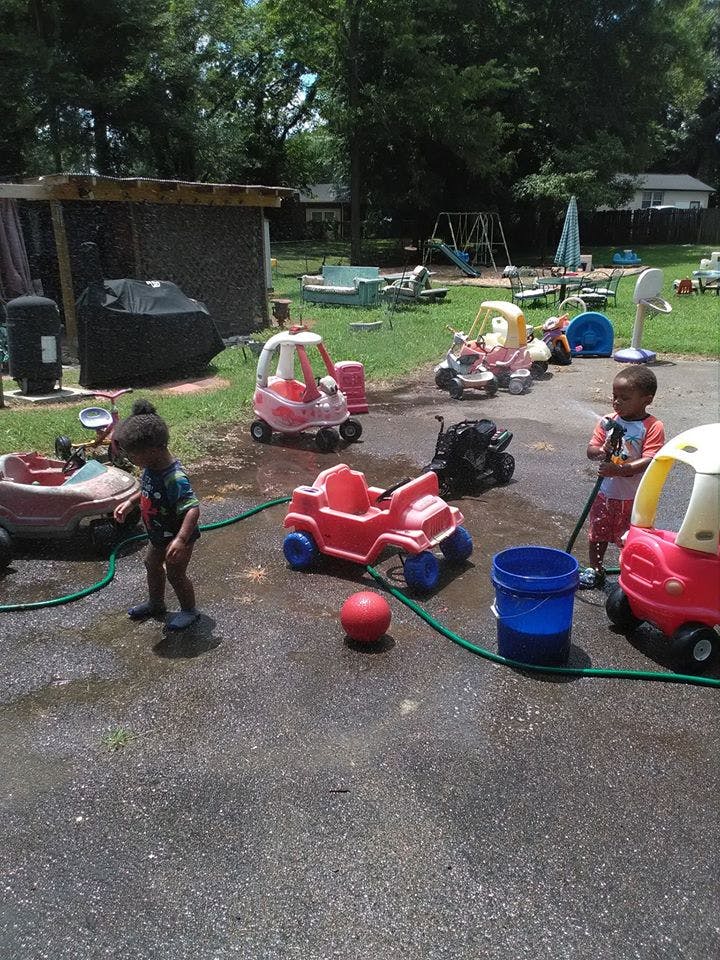 Two children playing with water hoses and toy cars outdoors