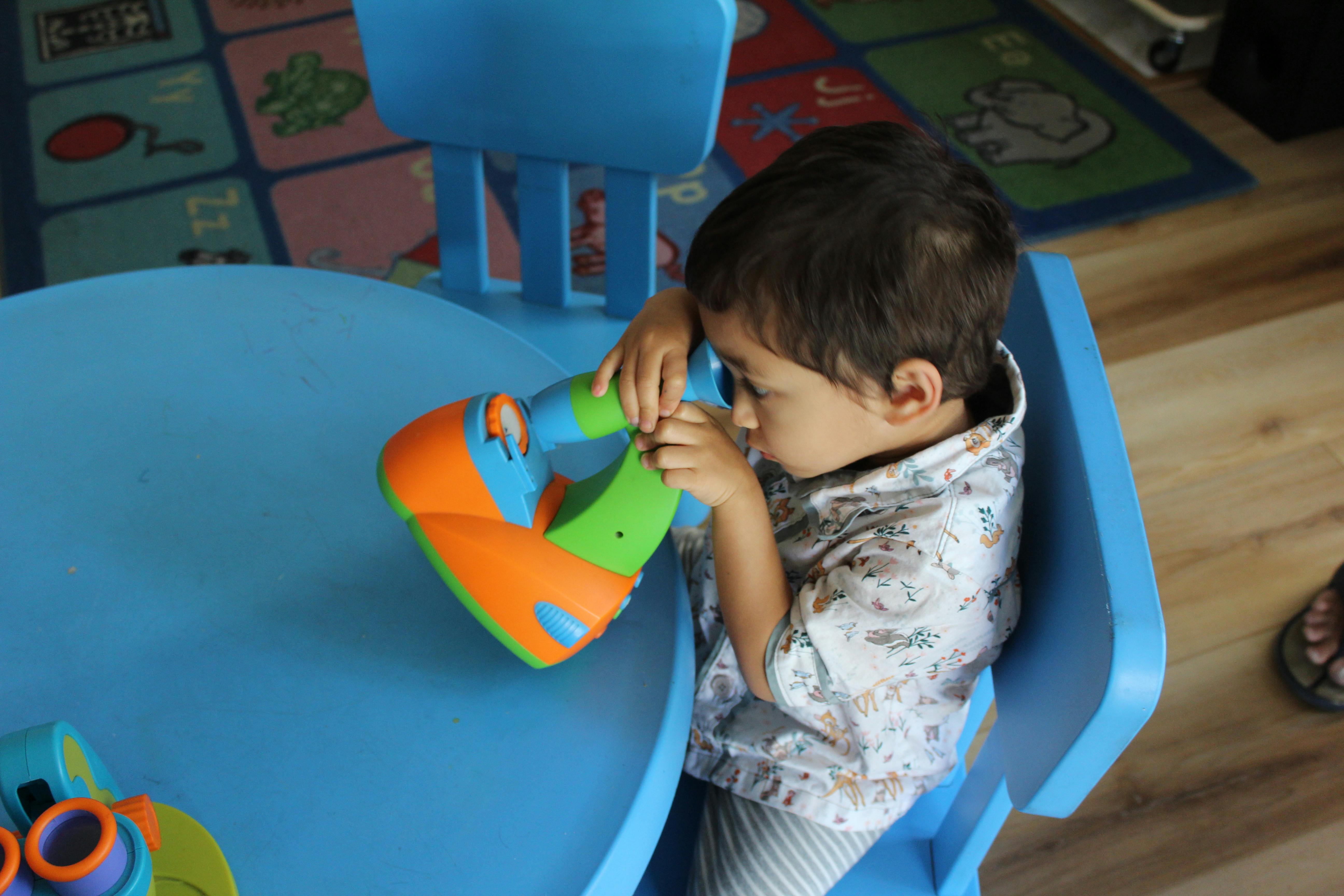 Child looking through a toy kaleidoscope at a blue table