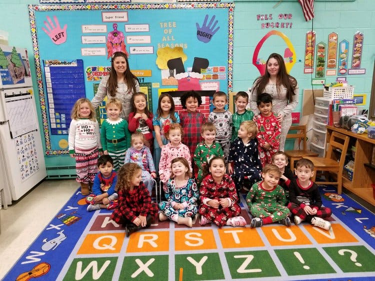 Two adults and many children in pajamas in a classroom